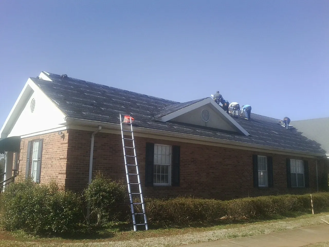 Crew tearing shingles off a brick ranch roof with a ladder set — Metal Roof Repair work by our crew in Truro
