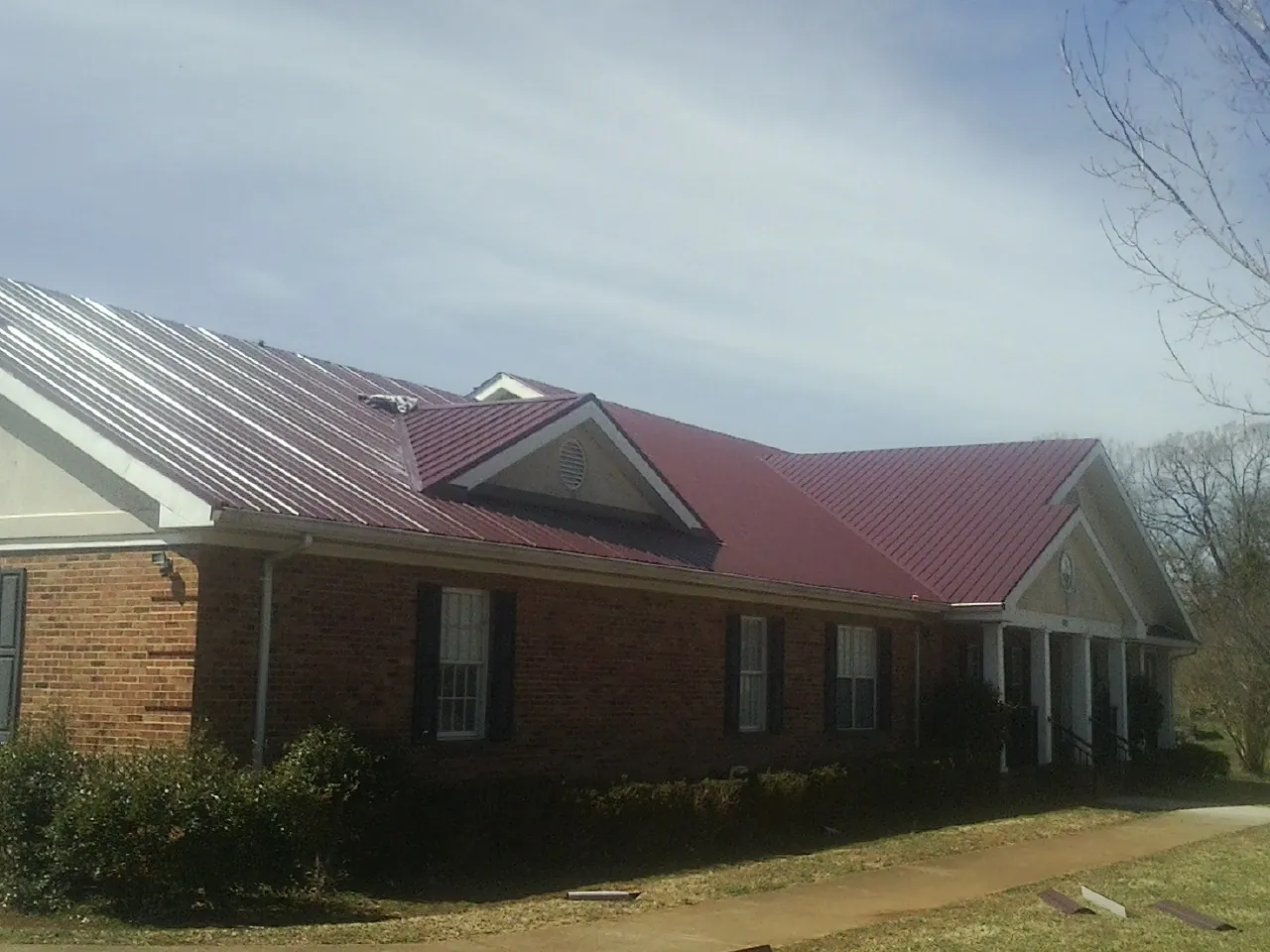 Red metal roof with gabled entries on a long brick building, from a Hail Damage Roof Repair job in Truro