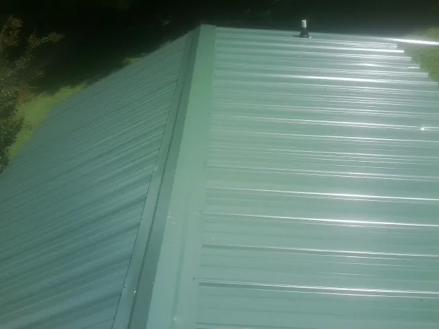 New green metal panels meeting at the ridge of a roof — Flat Roof Repair work by our crew in Truro