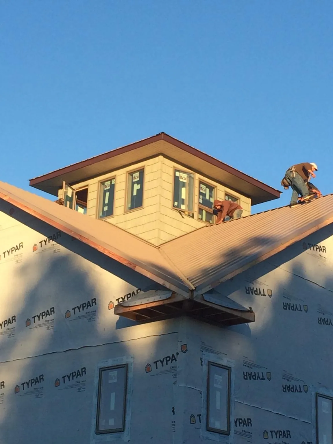 Roofers working around a rooftop cupola on a new metal roof at sunset — Roof Waterproofing in Truro by Roofing Brothers